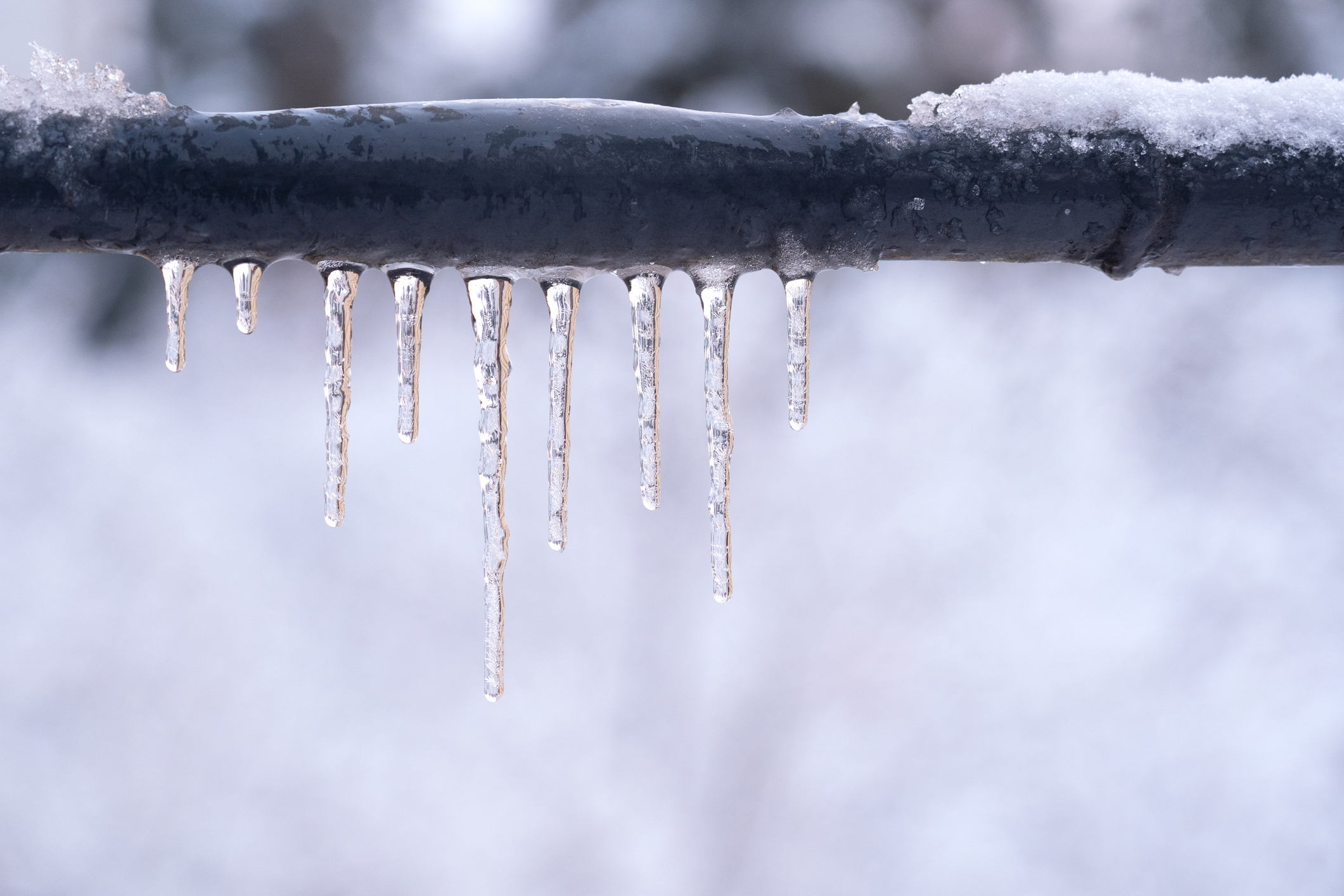 Frozen icicles on a gray pipe after a thaw in winter. Background. Form.